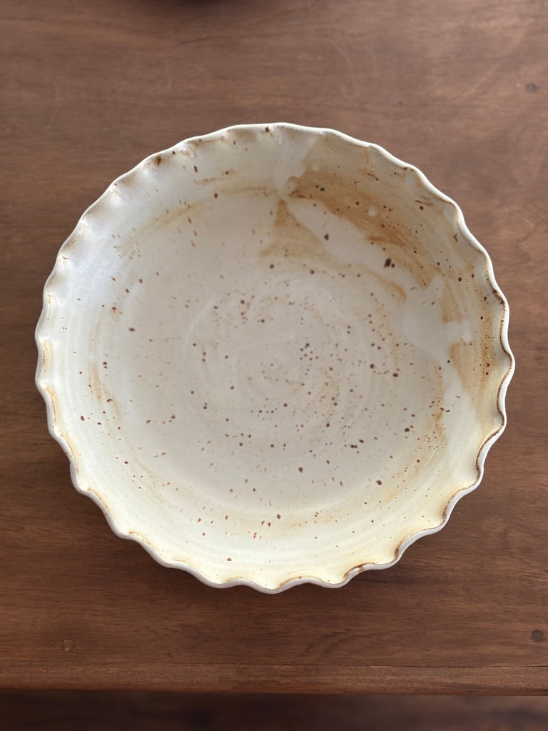 Large handmade white speckled pottery bowl with a ruffled rim, angled view